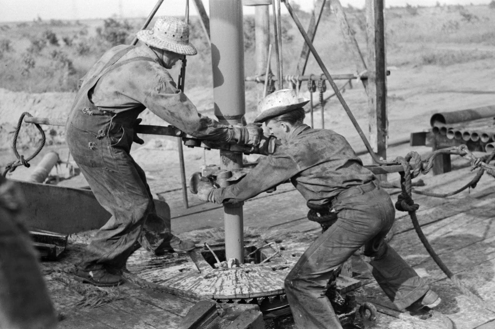 Russell Lee - Adding a length of drilling pipe at oil well in Seminole oil field, Oklahoma. Wrenches applied to loosen pipe, 1939